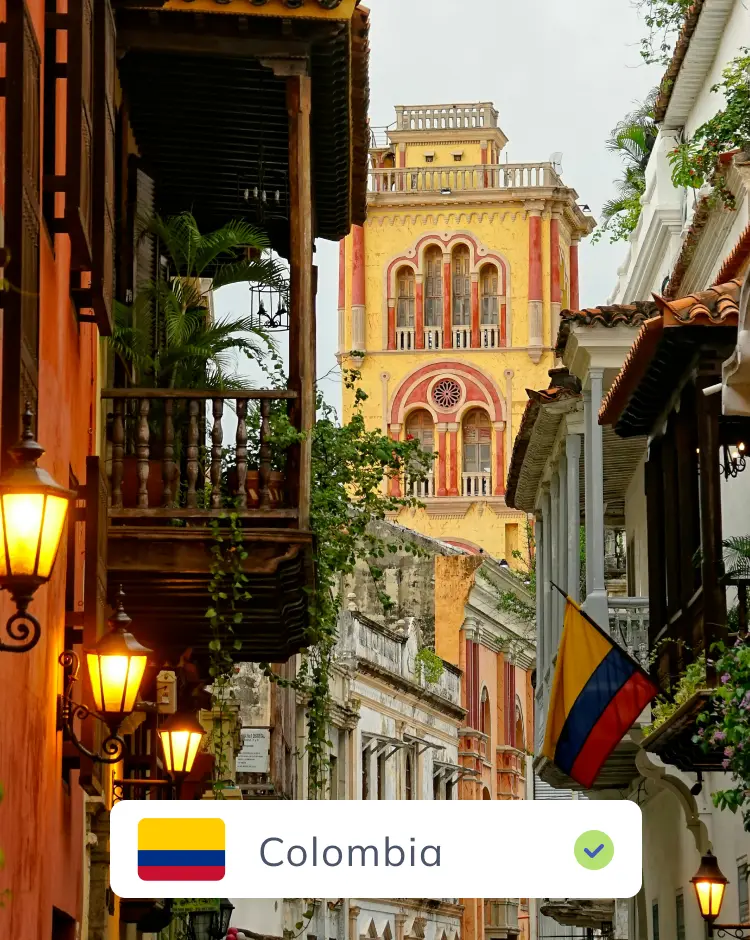 Street in Cartagena, Colombia framed by colorful colonial buildings, with a Colombian flag and a green checkmark indicating confirmed location.