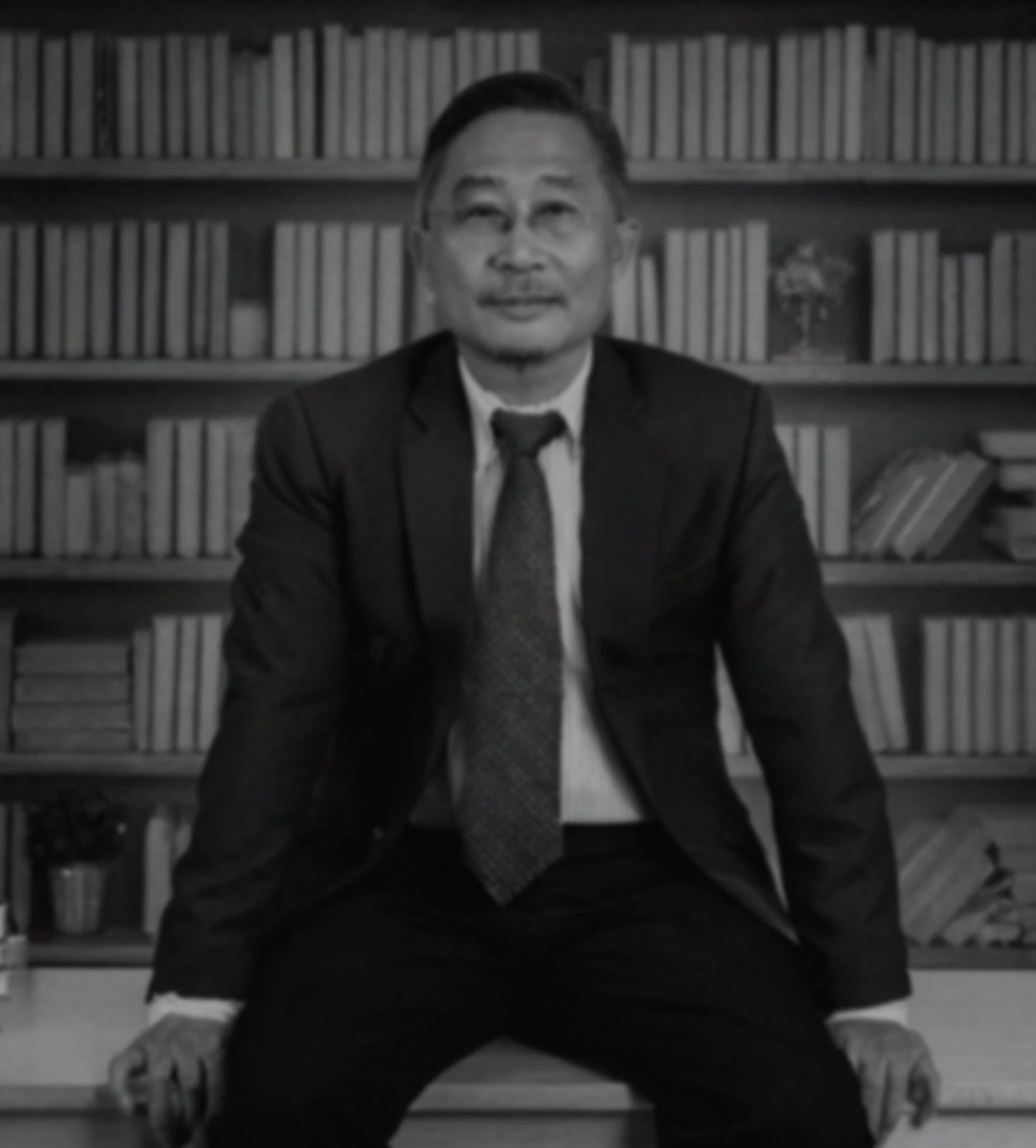 Portrait of a businessman in a suit, seated against a backdrop of books in his office.