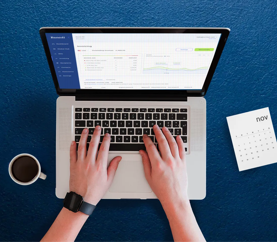 Overhead view of hands typing on a laptop displaying the Bancoli dashboard, with a notebook, pen, and calendar on a blue desk.